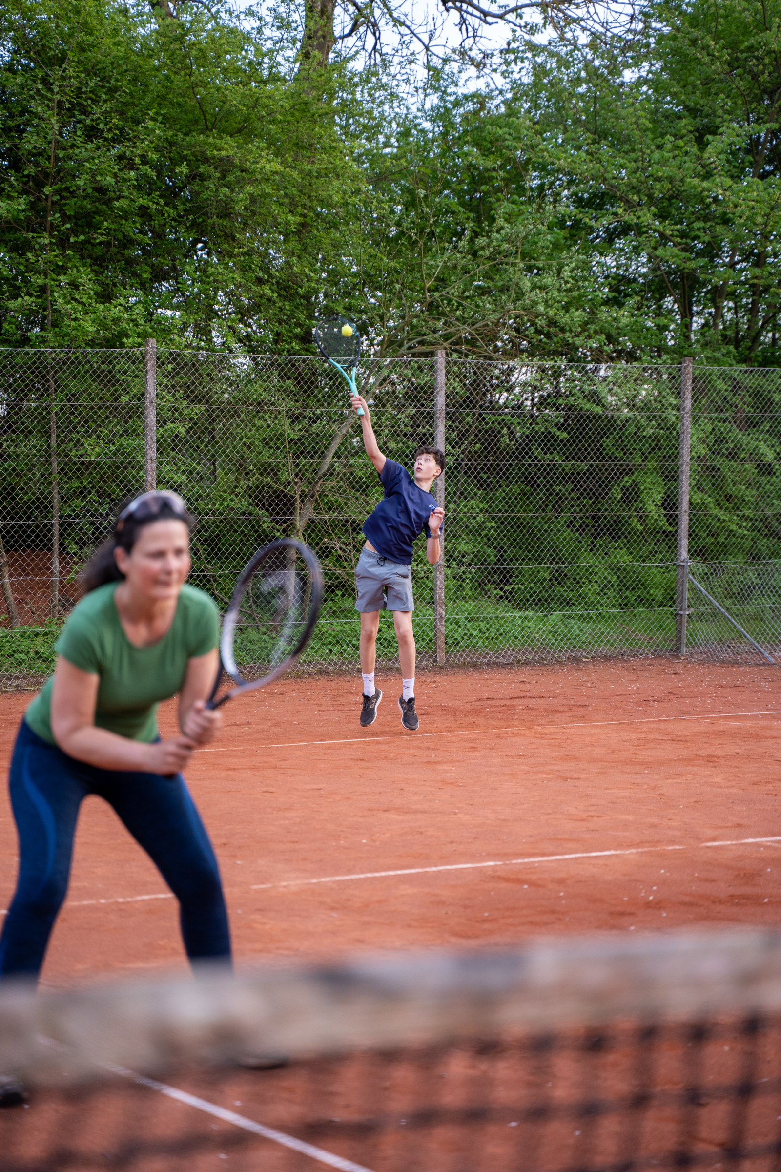 En voksen og en dreng spiller tennis på grusbanen